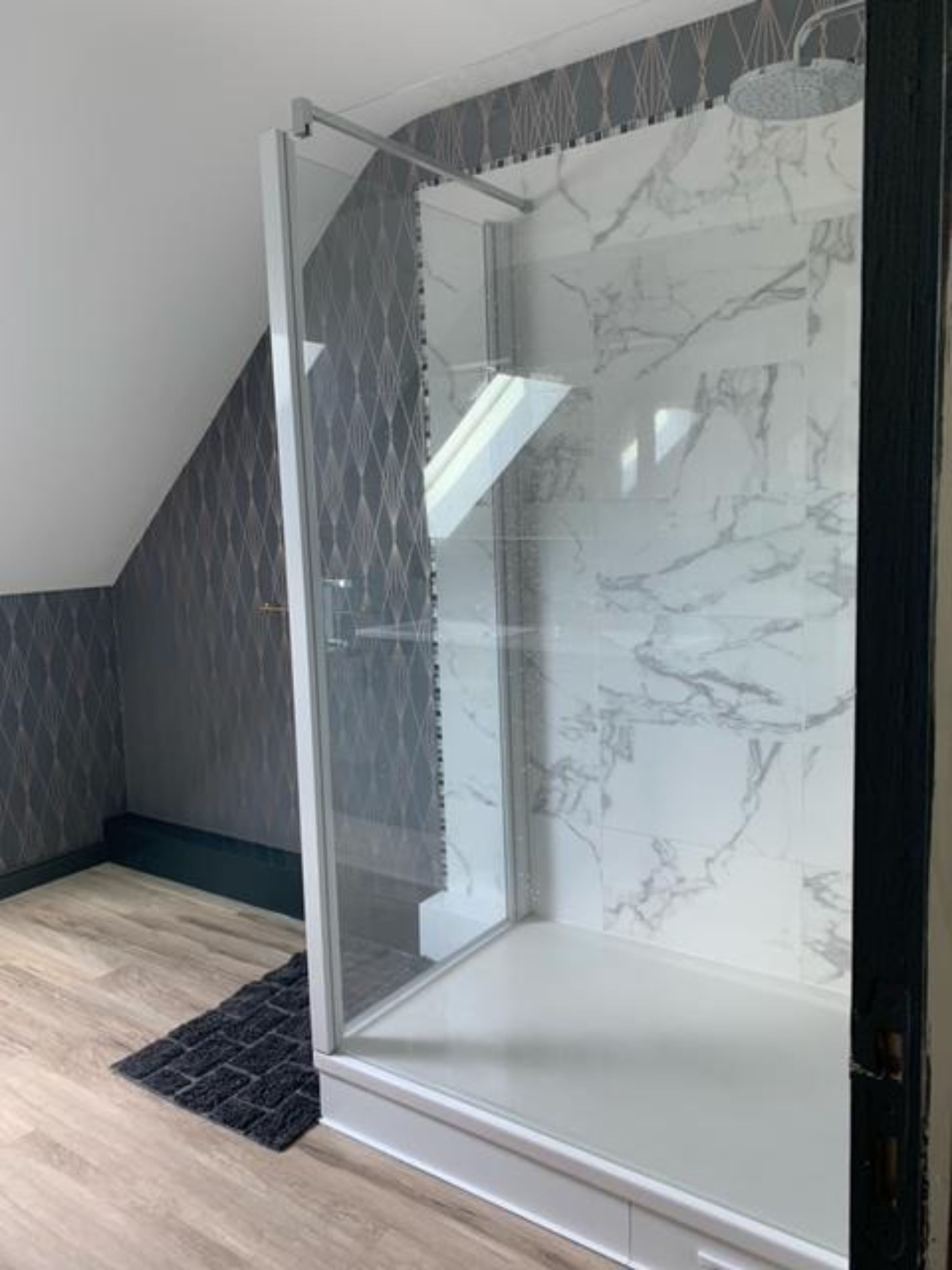 A modern shower enclosure with a glass door, marble tiles, and a dark patterned wall.