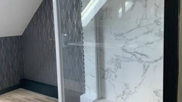 A modern shower enclosure with a glass door, marble tiles, and a dark patterned wall.