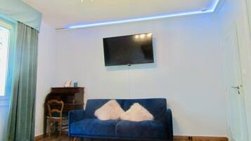 Una sala de estar con un sofá azul, una silla de madera, un televisor de pantalla plana montado en la pared y una araña.