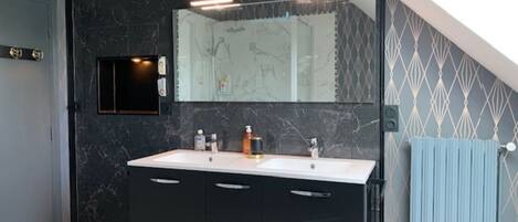 Un baño moderno con un revestimiento de mármol oscuro, un espejo grande y un mueble de tocador doble.