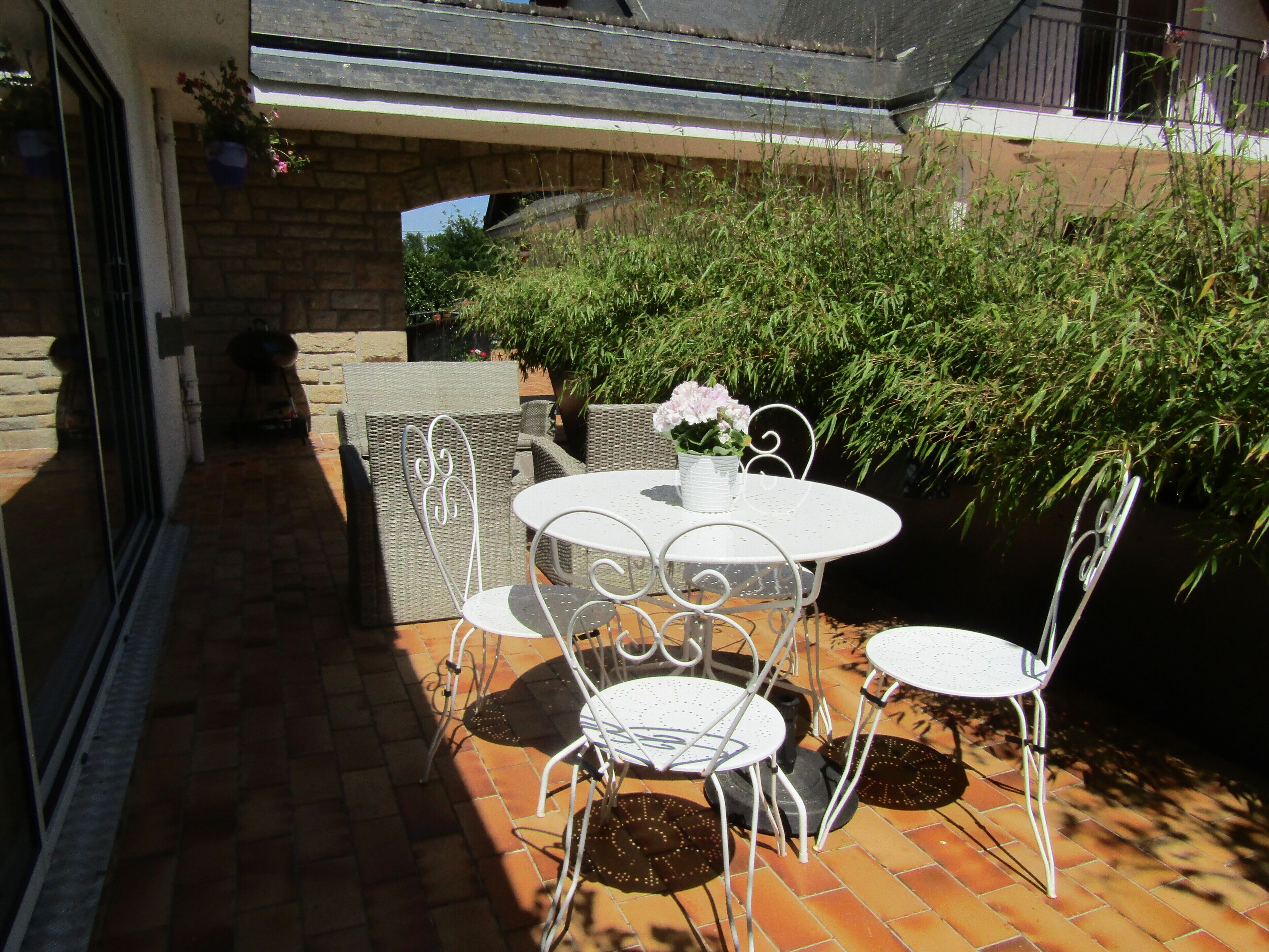 Un patio con una mesa redonda y cuatro sillas, rodeado de macetas con plantas y un muro de ladrillo.