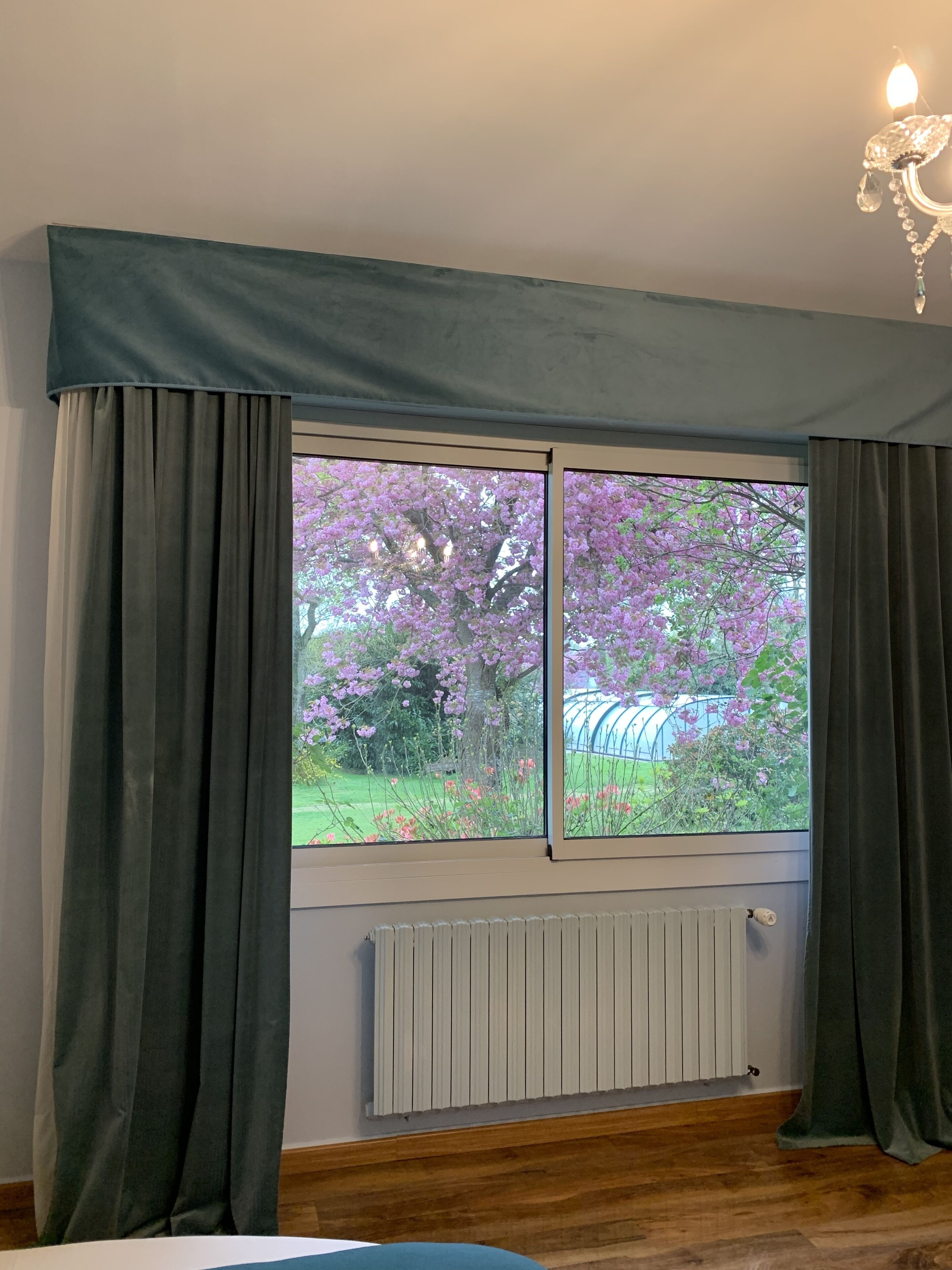 A room with a large window, dark curtains, a radiator, and a wooden floor.