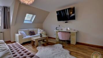 Un dormitorio tipo loft moderno con techo inclinado, un televisor de pantalla plana grande, un sofá blanco, una silla rosa, una mesa de centro de madera y una alfombra blanca mullida.