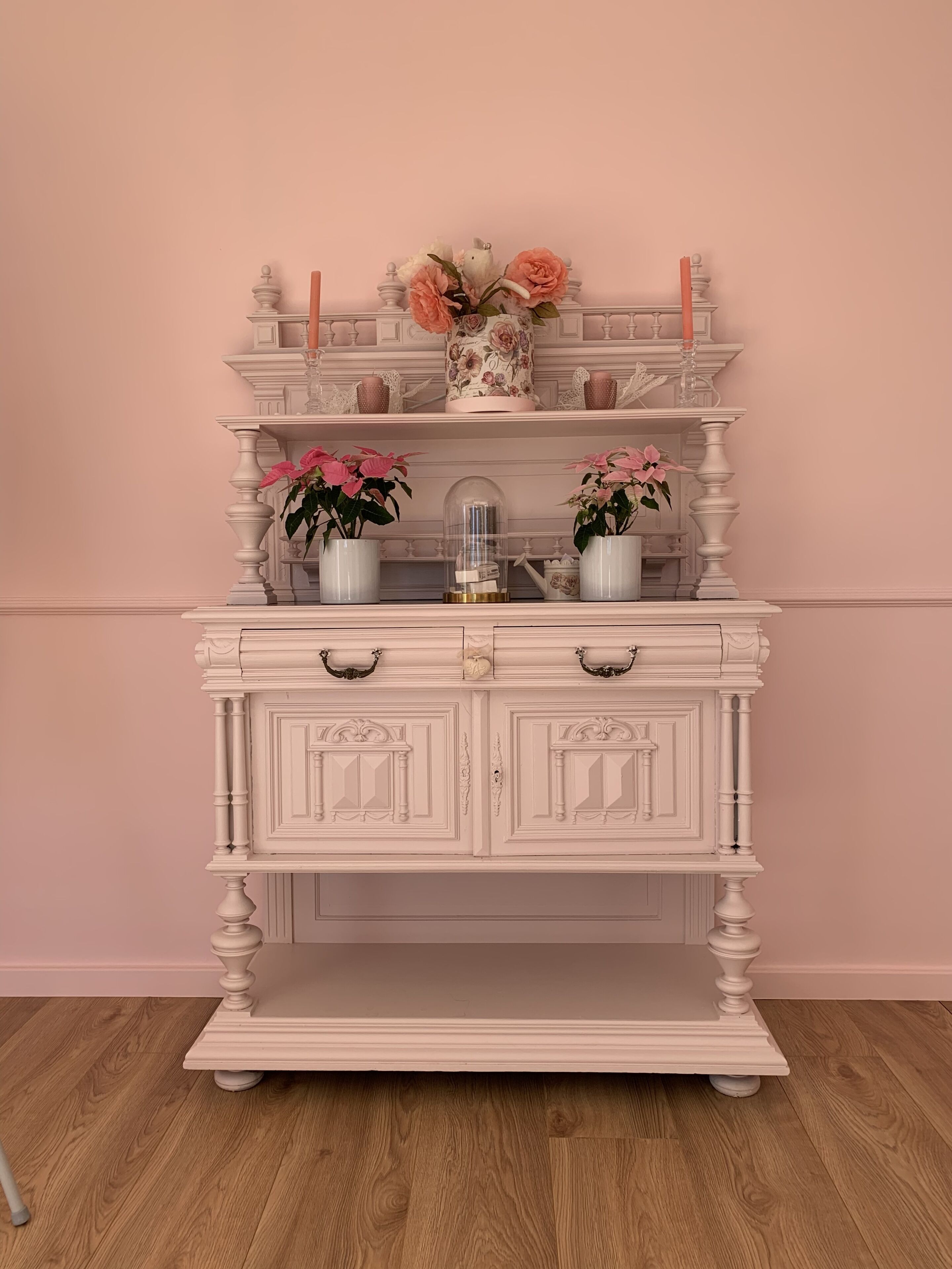 Un elegante tocador blanco con dos cajones y una superficie de vidrio, decorado con flores rosadas y un florero.