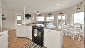 A spacious kitchen with white cabinets, a black stove, and a dining area with white chairs and a table.