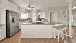 A modern kitchen with white cabinetry, a stainless steel refrigerator, a central island with stools, and a ceiling fan.