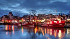 Een havenzicht met verschillende boten afgemeerd aan een steiger, omringd door gebouwen met verlichte borden en lichtreflecties op het water.
