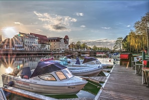 A marina with boats docked, a wooden pier, and buildings in the background.