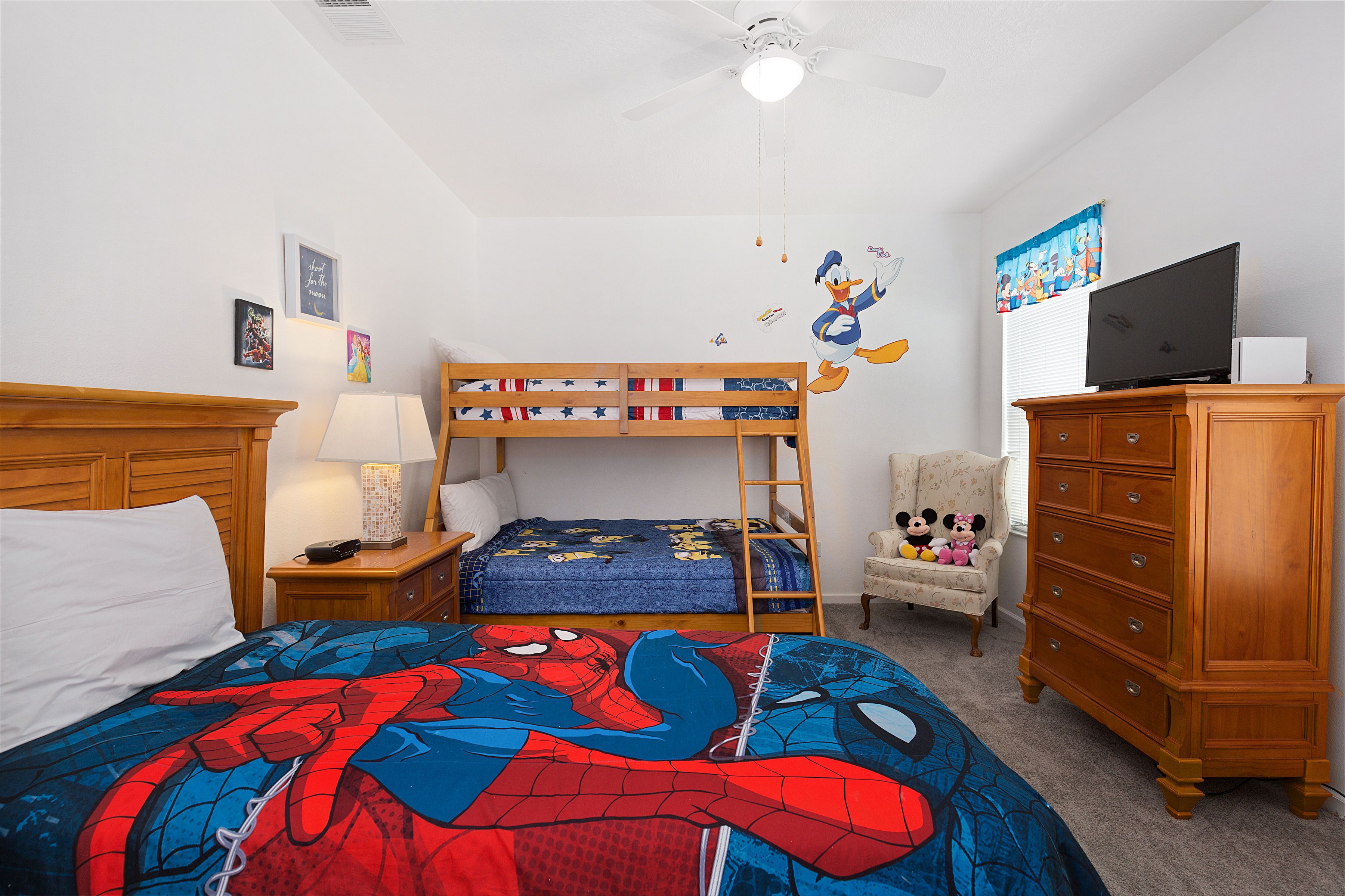 A bedroom with a bunk bed, a desk with a lamp, a dresser, and a television.