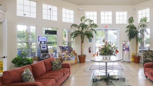 A spacious lobby with a red sofa, a glass coffee table, and potted plants. - Our Happy Place by VillaDirect (Kissimmee)