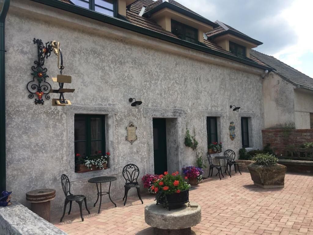 Um edifício com fachada rústica, área externa com mesas e cadeiras, e vasos de flores.