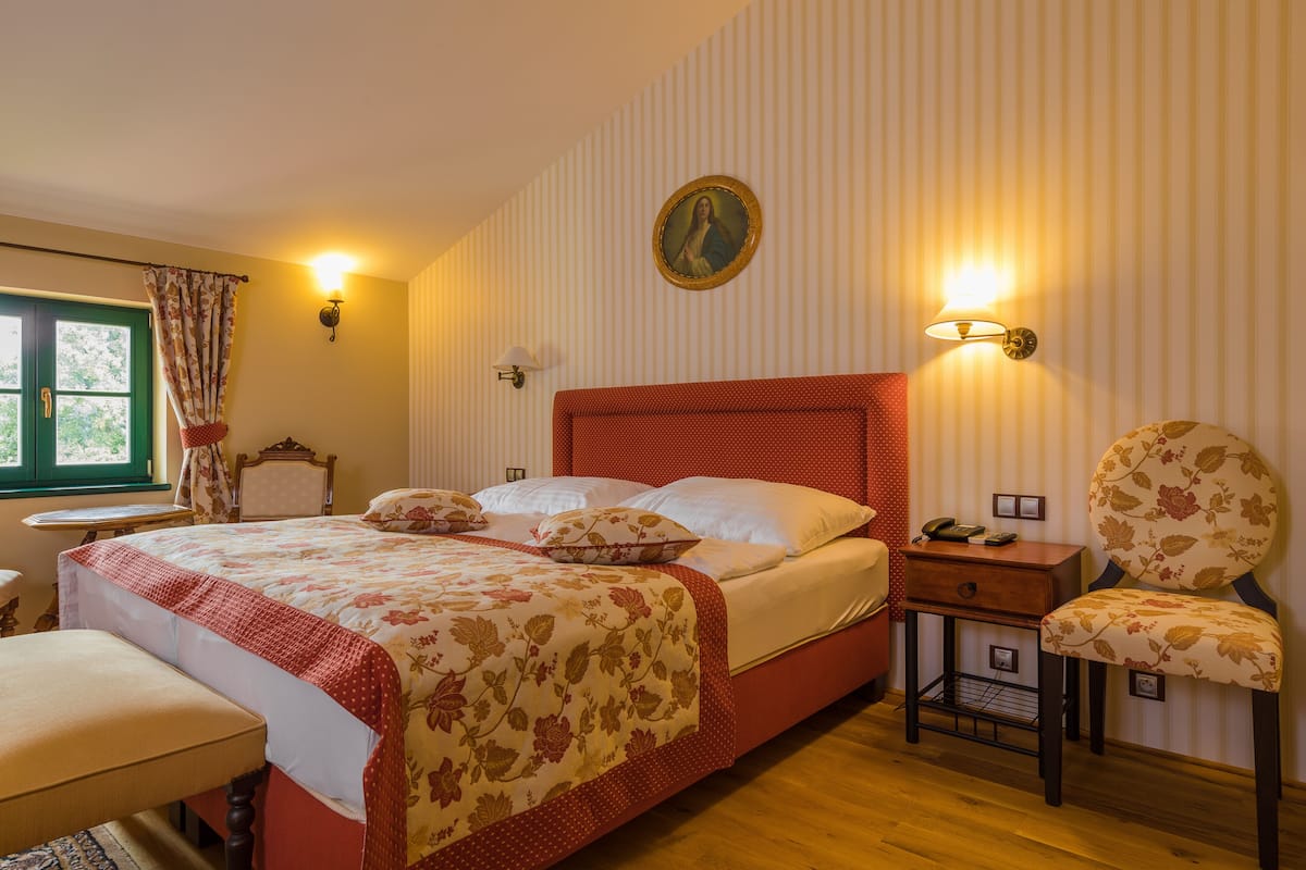 Un dormitorio con una cama grande, una silla, una mesita de noche y una lámpara de pared.