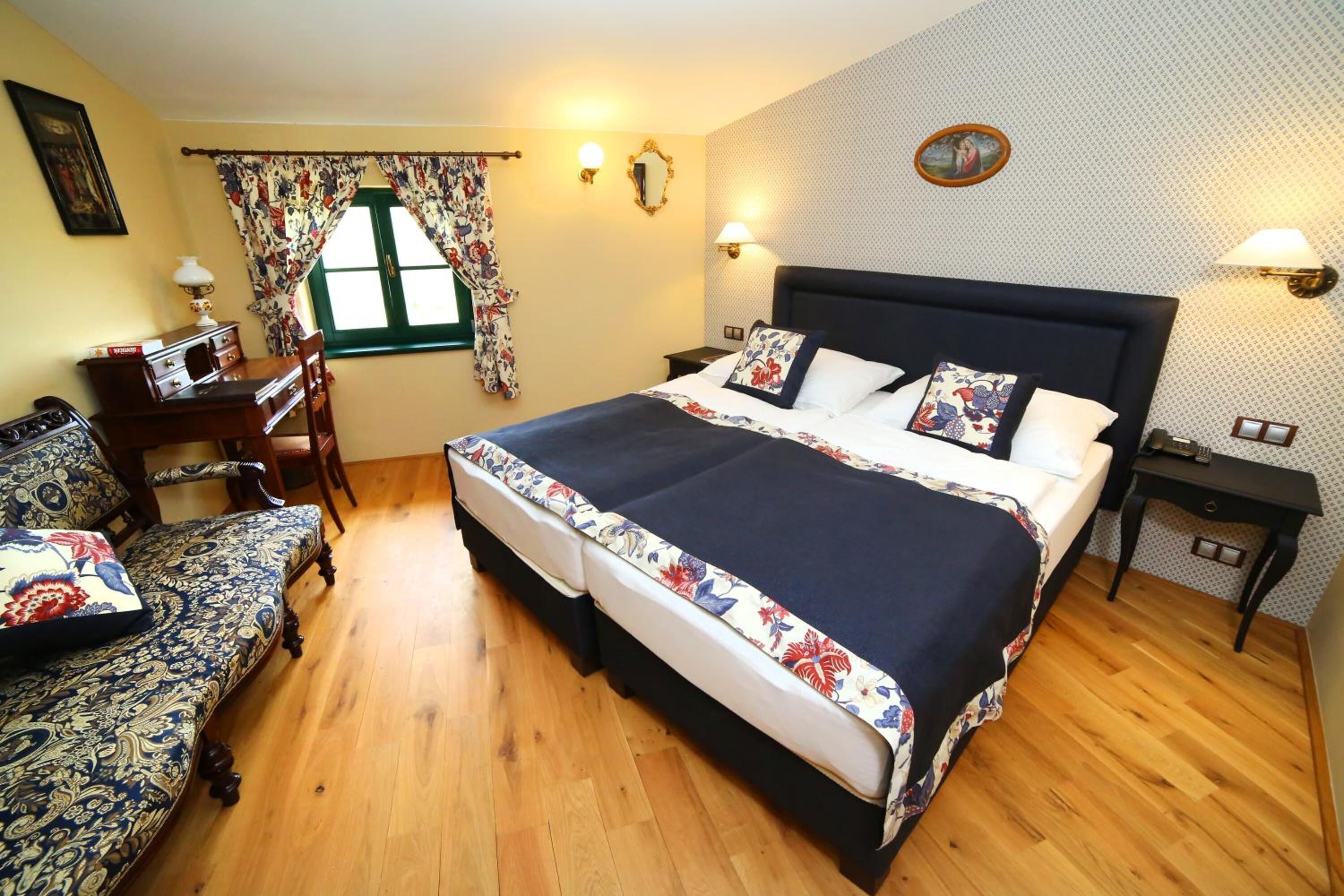 Un dormitorio con una cama grande, un escritorio de madera, una silla y un ventanal con cortinas florales.