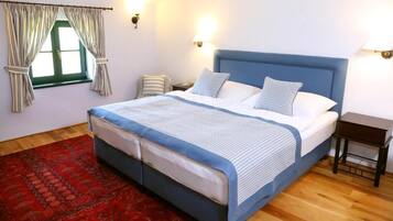 A bedroom with a bed, a nightstand, a lamp, a window with curtains, and a red carpet.