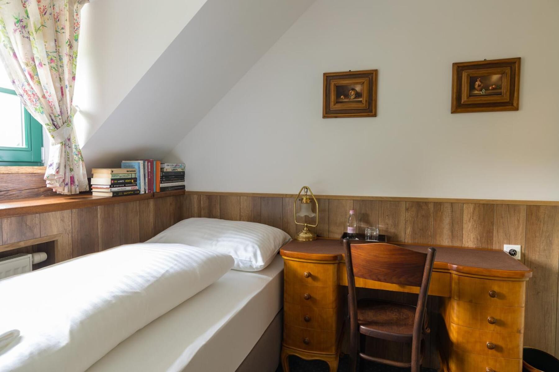 Un dormitorio con cama, escritorio de madera, silla, libros y dos cuadros en la pared.