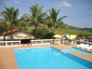 Una piscina con valla blanca, palmeras y vistas al campo.