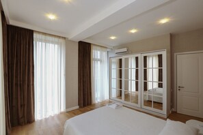 A hotel room with a large bed, a wardrobe, a sliding glass door leading to a balcony, and an air conditioning unit on the wall. - Hosthub - 2BR Super view Apartment (Tbilisi)
