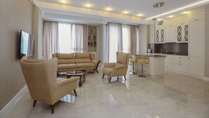 A modern living room with a sofa, armchairs, a coffee table, and a TV. It features a kitchen with white cabinets and a dining area. - Hosthub - 2BR Super view Apartment (Tbilisi)
