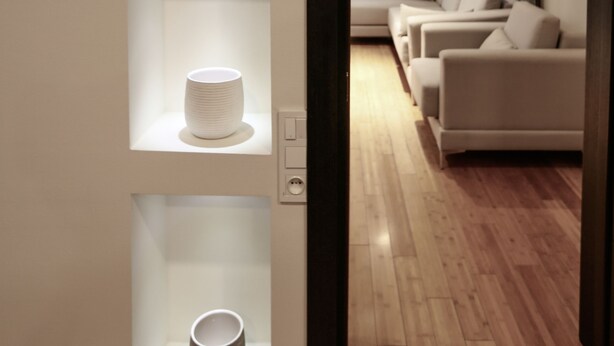 Un interior moderno con suelo de madera, un conjunto de sofá blanco y estantes con objetos decorativos.