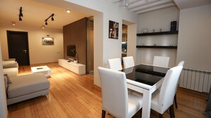 Un salón moderno con comedor, suelo de madera, muebles blancos e iluminación empotrada.