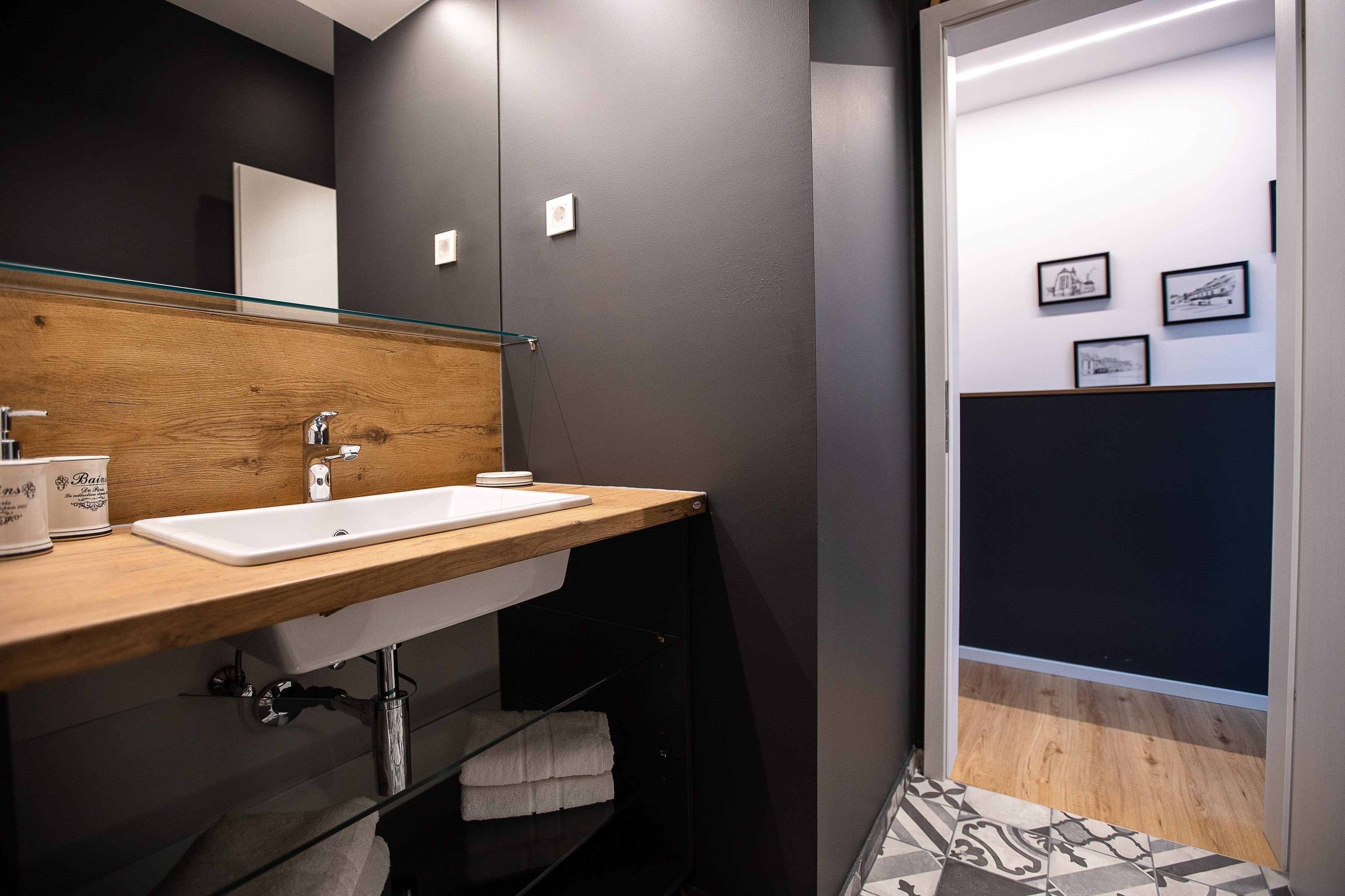 Un baño moderno con tocador de madera, un lavabo blanco y mampara de ducha de vidrio.