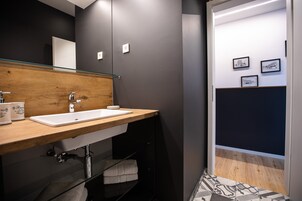 Un baño moderno con tocador de madera, un lavabo blanco y mampara de ducha de vidrio.
