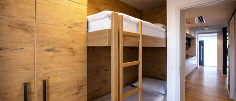 Una cama litera con escalera, un armario de madera y un pasillo que conduce a otra habitación.