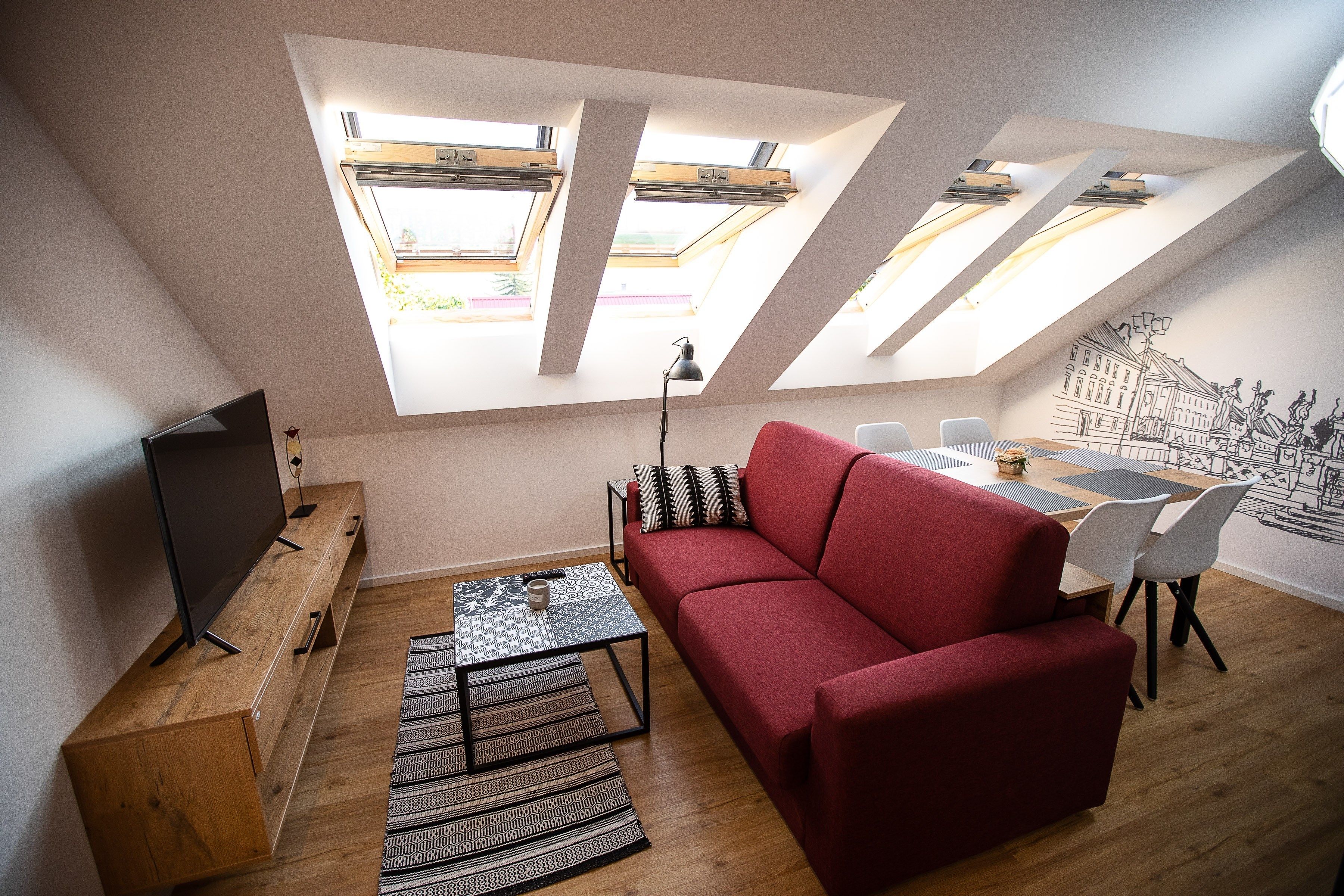 Una sala de estar moderna con un sofá rojo, un televisor sobre un mueble de madera, una zona de comedor con sillas y tragaluces.