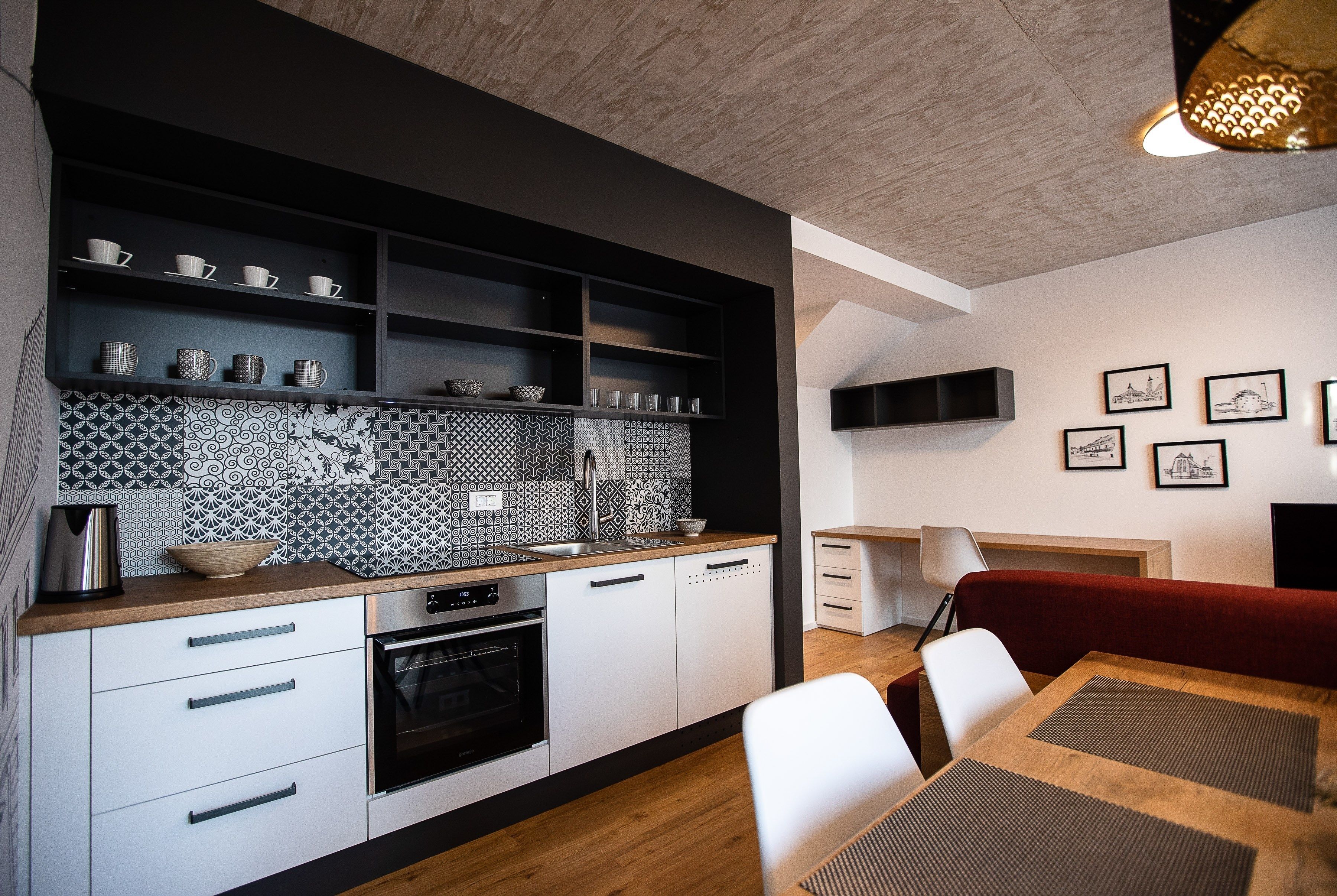 A modern kitchen with white cabinetry, a patterned backsplash, and a dining area with a red sofa and white chairs.