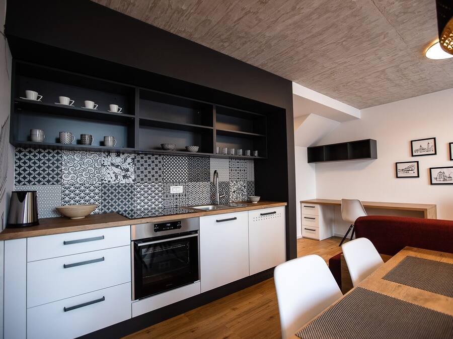 A modern kitchen with white cabinetry, a patterned backsplash, and a dining area with a red sofa and white chairs.