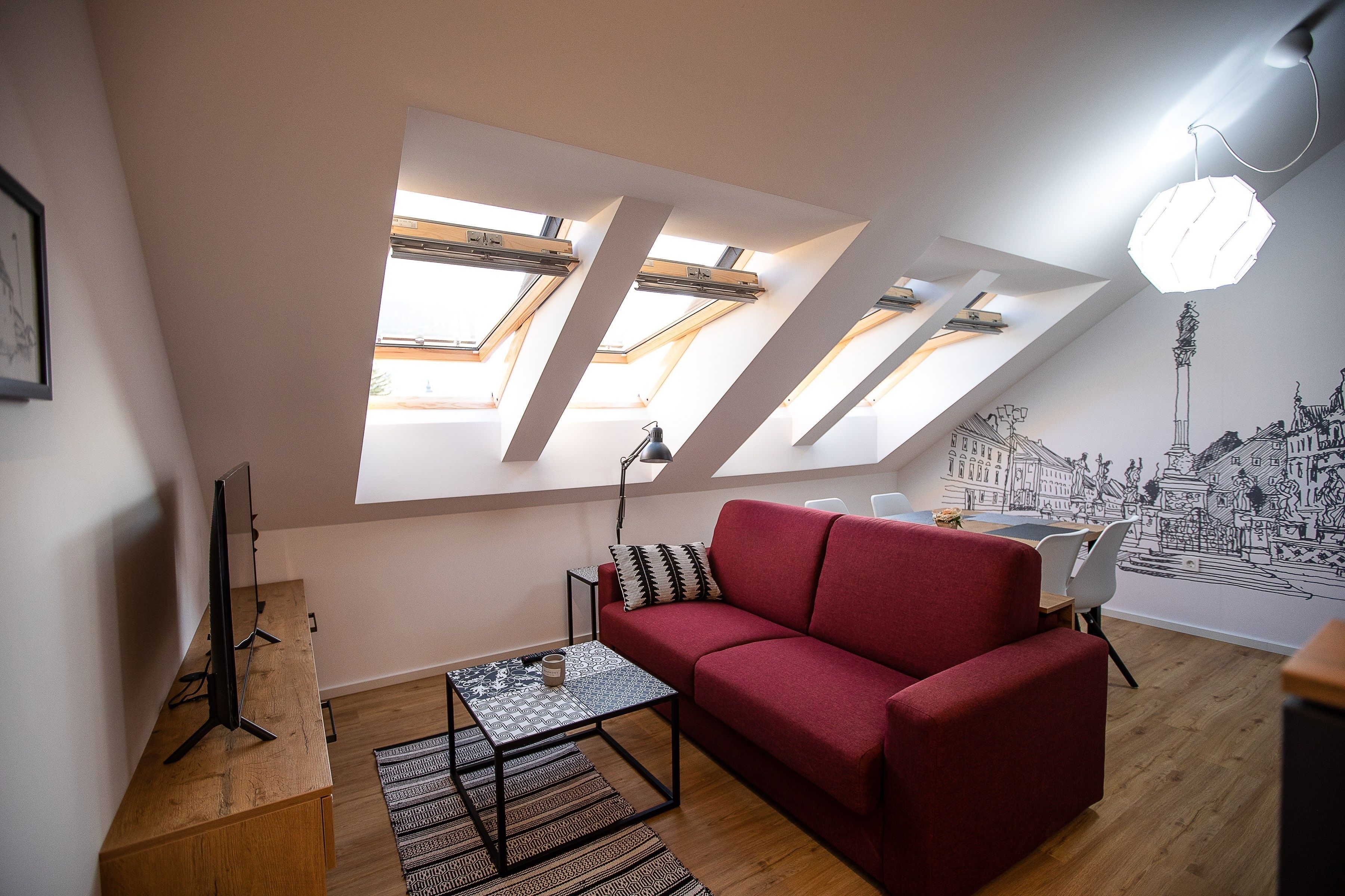 Ett modernt vardagsrum med en röd soffa, ett soffbord och en väggmålning som föreställer en stadsbild.