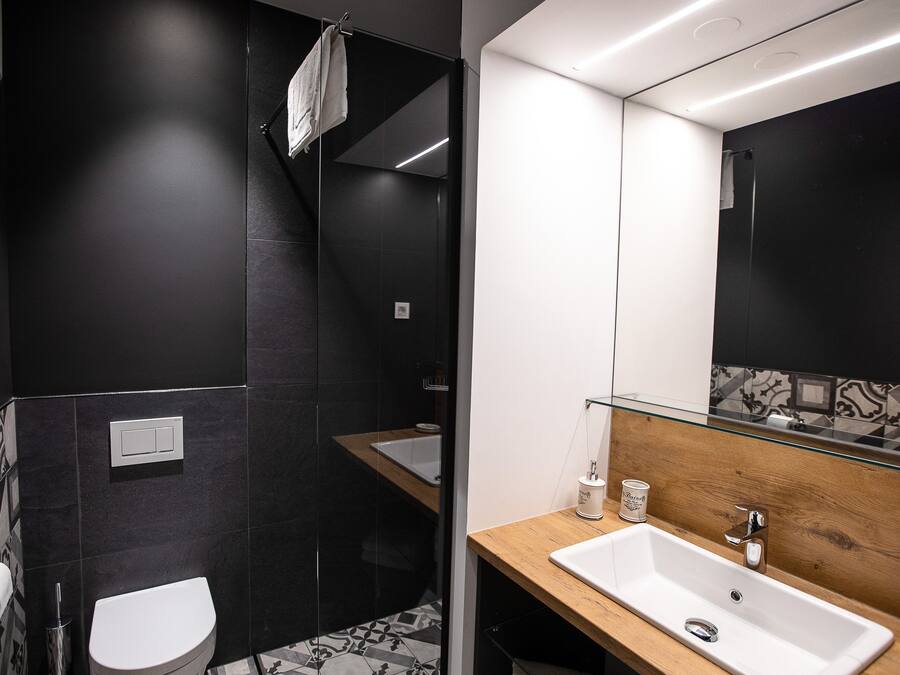 A modern bathroom with a white toilet, a glass shower enclosure, a wooden vanity with a white sink, and a large mirror.