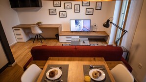 Ein moderner Wohnraum mit Essbereich, einem roten Sofa, einem Holztisch, einem Fernseher und gerahmten Bildern an der Wand.
