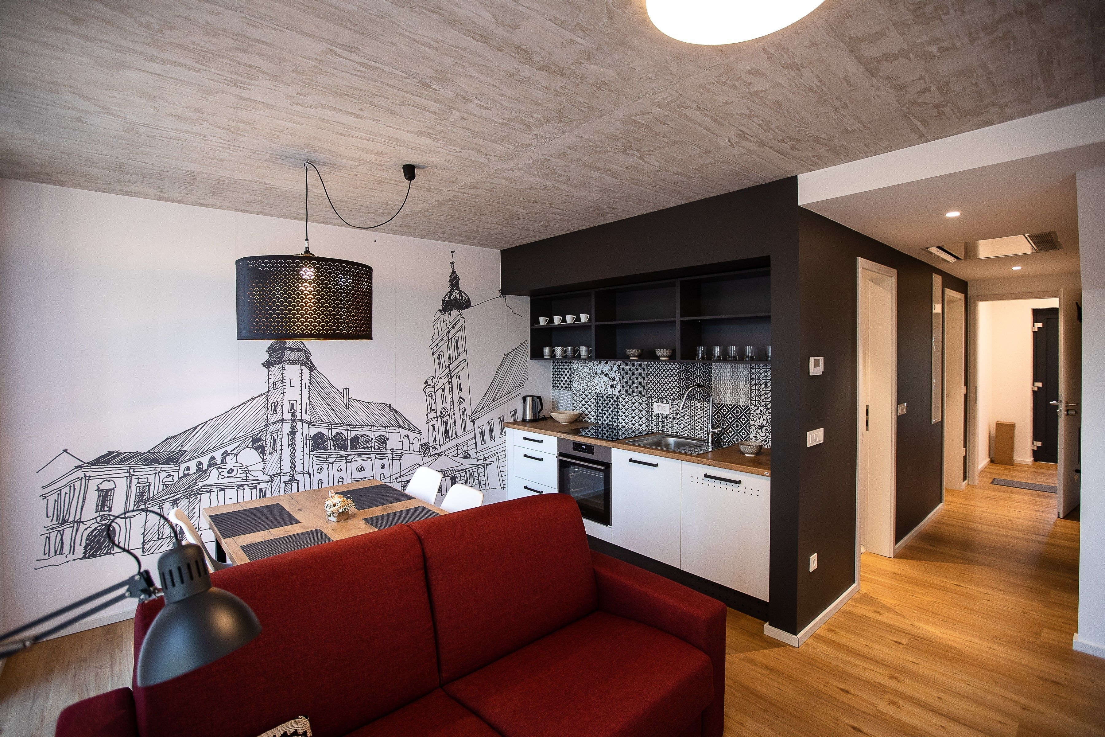 A modern kitchen with a dining area, featuring a red sofa, a wall-mounted lamp, and a kitchen island.