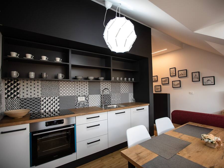 Cozinha moderna com forno embutido, bancada de madeira e painel de fundo preto. Há uma área de refeições com mesa e cadeiras de madeira, e um sofá vermelho.