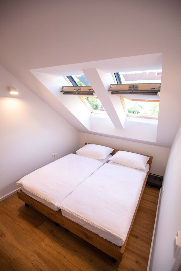 A bedroom with a skylight, wooden bed frame, and white bedding. - Postcard City Apartments (Maribor)