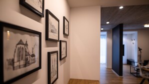 Ein Flur mit gerahmten architektonischen Zeichnungen an der Wand, einer hölzernen Bank und einem modernen Interieur mit Akzentwand in dunkler Farbe und Einbauleuchten.