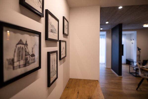 Un couloir orné de reproductions d’anciens plans d’architecture, un banc en bois et un intérieur moderne avec un mur d’accent de couleur sombre et un éclairage encastré.