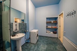 A compact bathroom with a sink, washing machine, and shelves with toiletries.