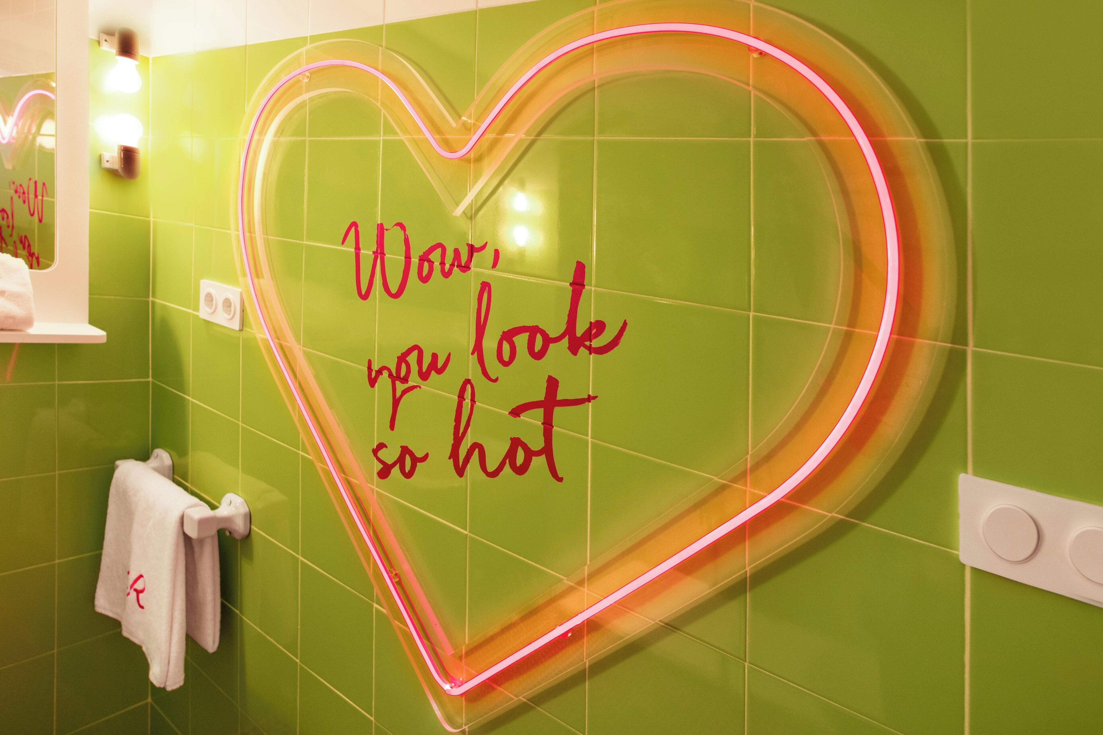 Un baño con un letrero luminoso en forma de corazón y un perchero.