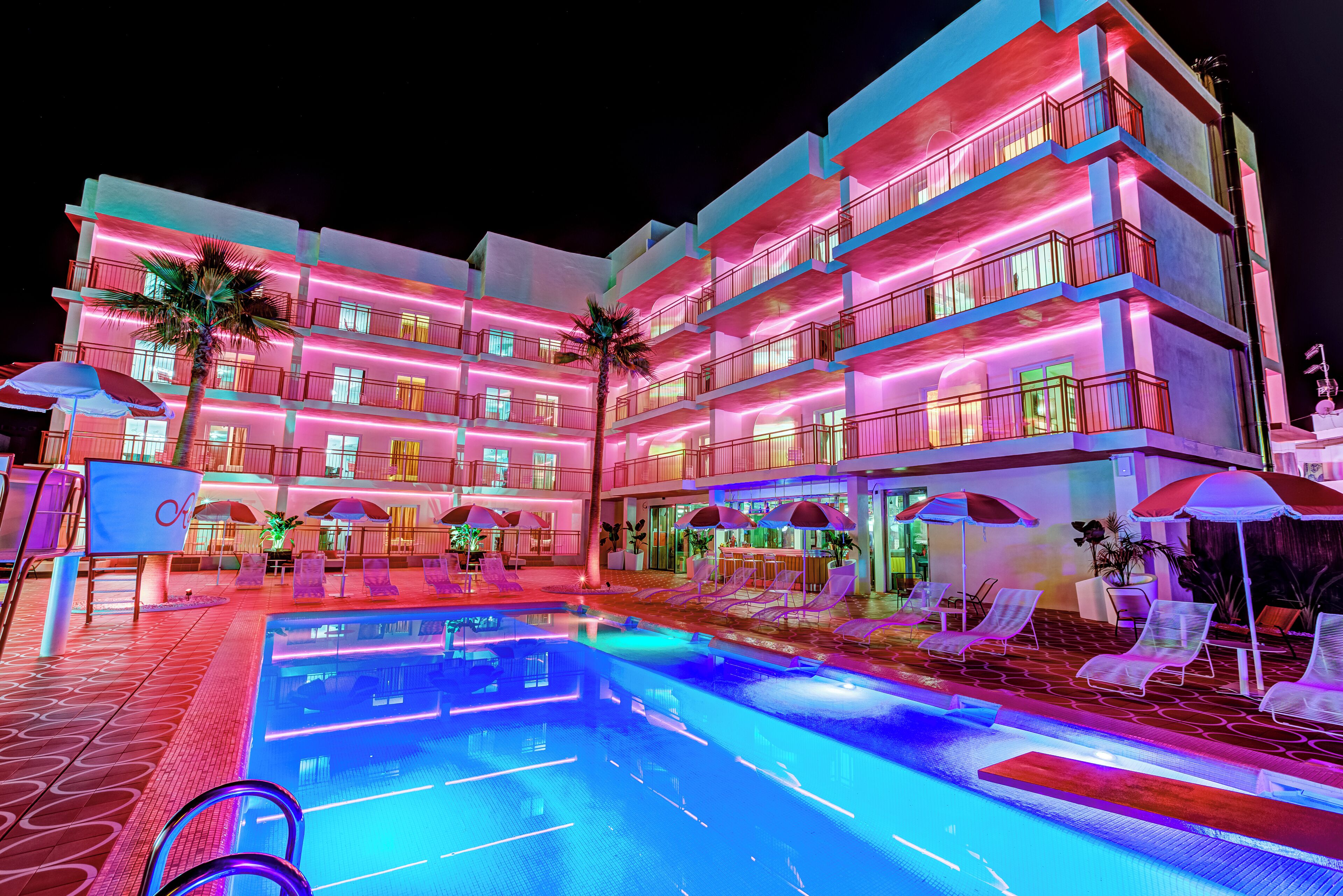 Ein mehrstöckiges Hotel mit Poolbereich, einschließlich Liegestühlen und Sonnenschirmen.