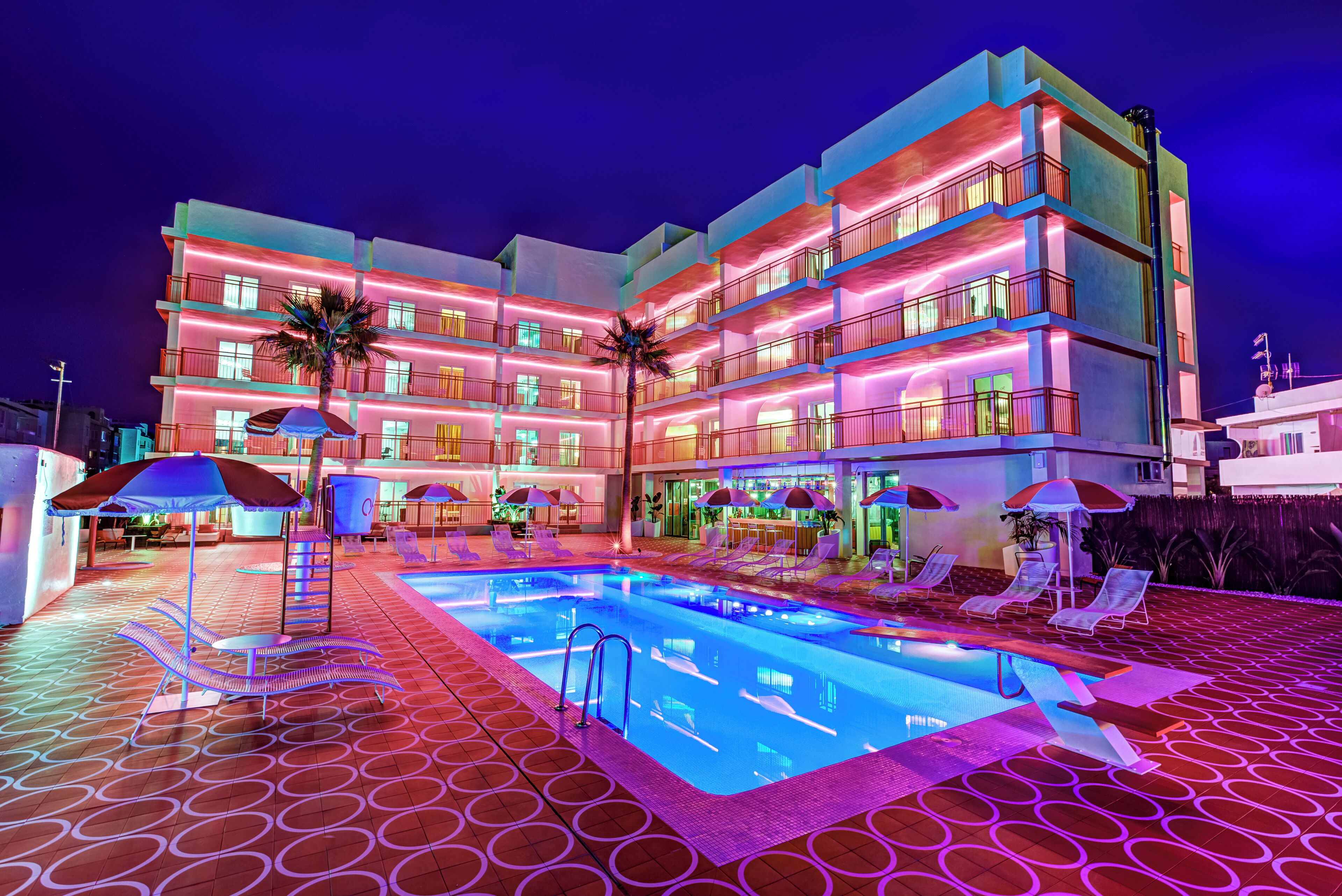 A multi-story hotel with a swimming pool, outdoor seating, and palm trees.