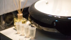 A bathroom with a large black sink, a bottle of reed diffuser, and three tubes of Aquiline body lotion. - Apartment Le Soleil (Tbilisi)