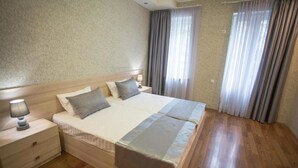 A hotel room with a large bed, wooden nightstands, a lamp, and curtains. - Apartment Le Soleil (Tbilisi)