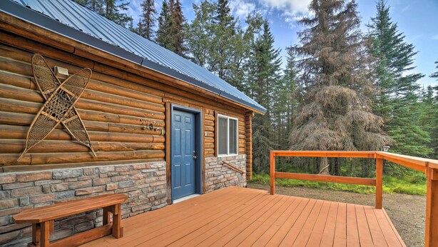 Una cabaña de troncos con cimientos de piedra, una puerta azul y una terraza de madera.