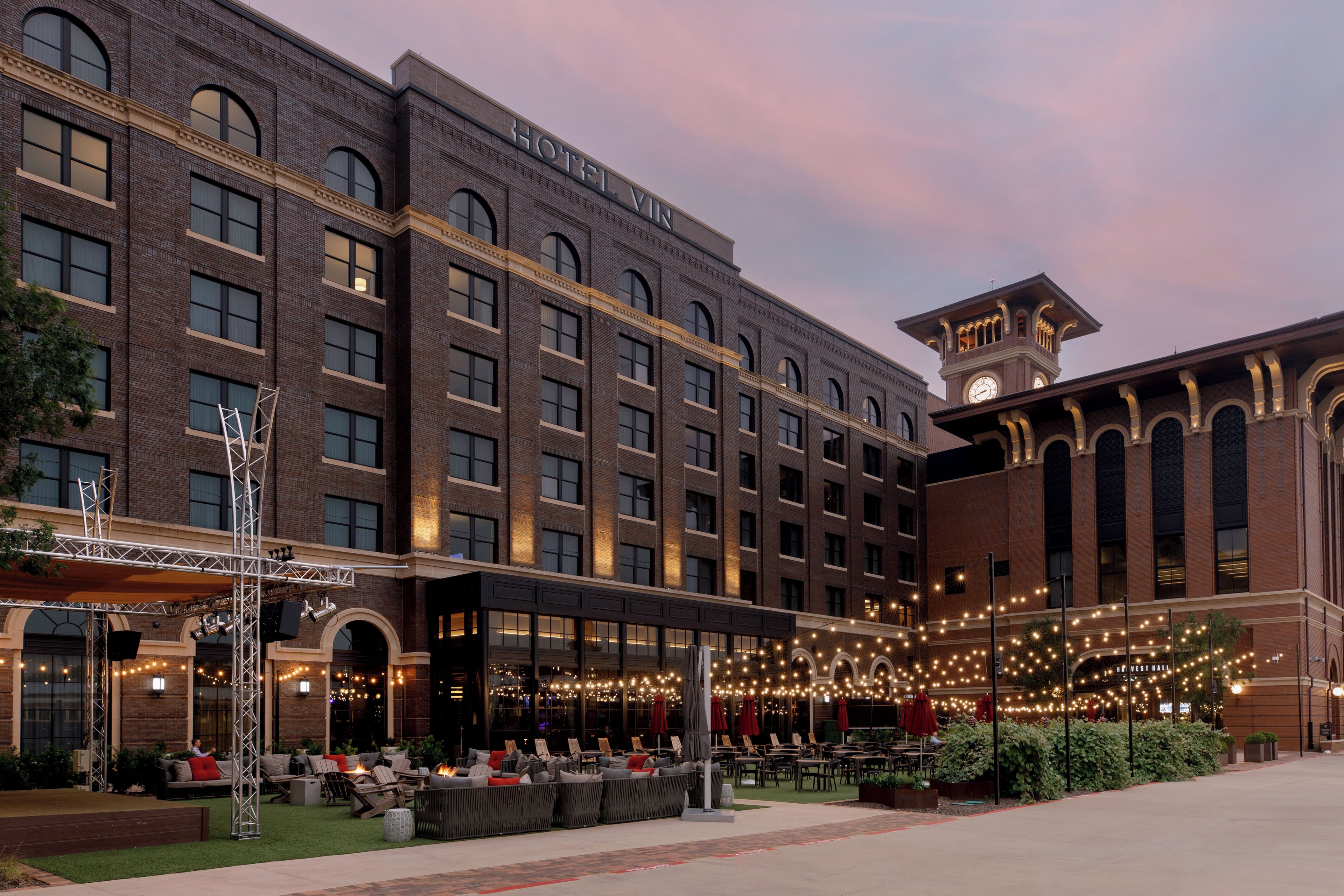 A hotel with a brick facade, multiple windows, and a covered outdoor seating area with string lights.