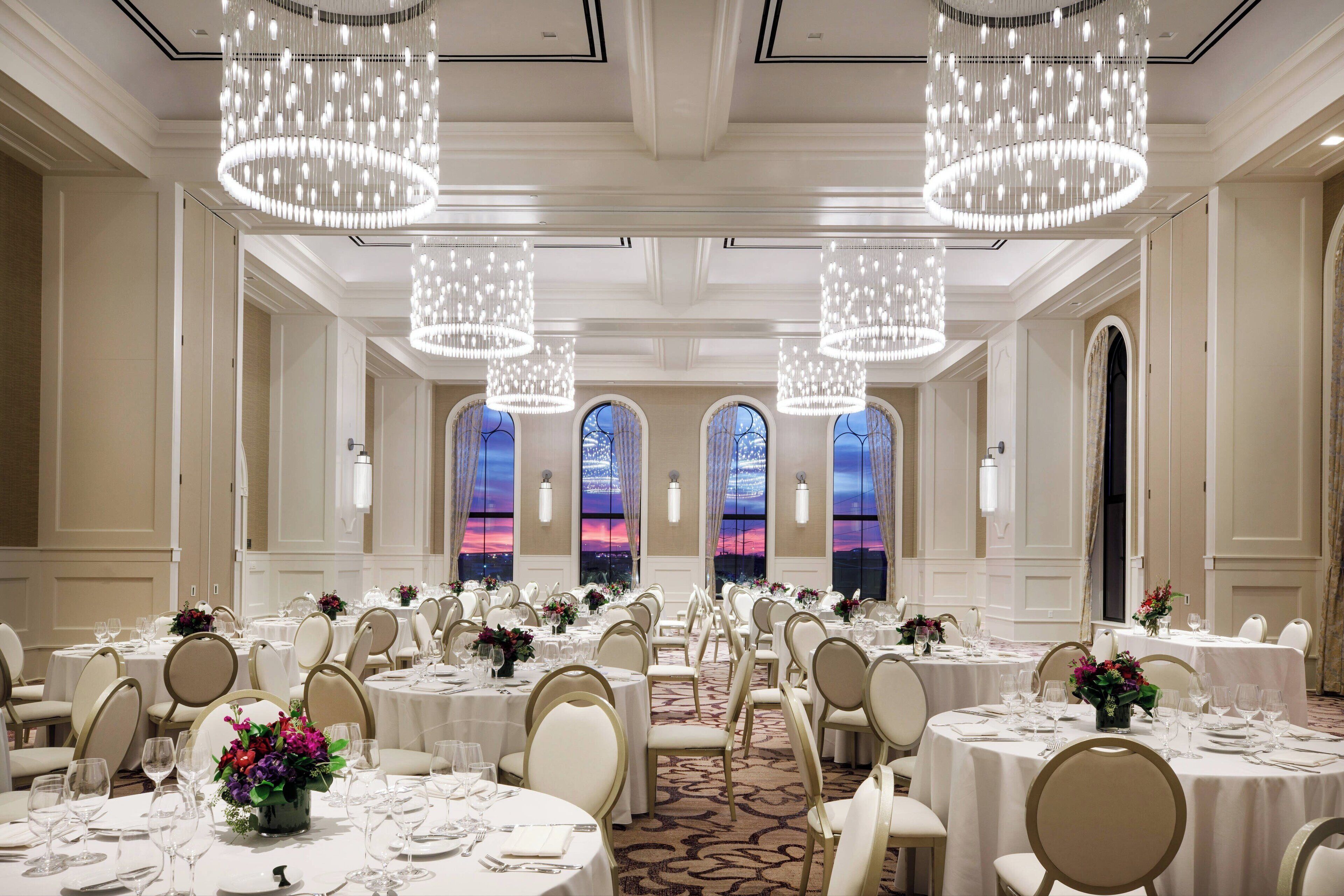 Un salón de banquetes con mesas redondas, manteles blancos y candelabros.