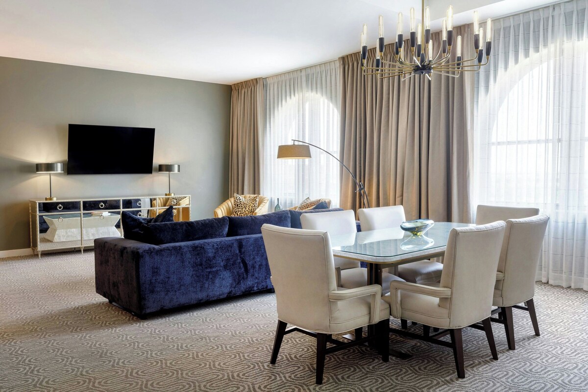 A modern living room with a blue sofa, a glass dining table, and white chairs.