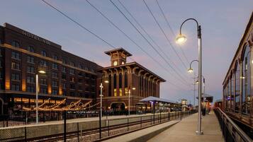 A hotel with a clock tower, a covered outdoor seating area, and a view of the train station.