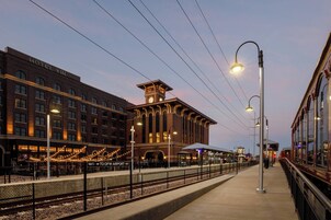 A hotel with a clock tower, a covered outdoor seating area, and a view of the train station.